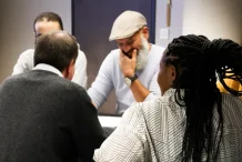 Homme au béret souriant lors d'une discussion d'équipe.